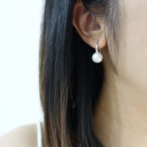 A close-up lifestyle shot of a model wearing the Luna Pearl Sterling Silver Ear Hooks, showcasing the large 10mm freshwater pearls with a high-lustre finish against a professional, clean-cut look.
