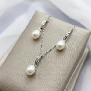 A pair of minimalist swaying drop earrings featuring genuine white freshwater rice pearls suspended from 925 sterling silver settings with premium 18K gold plating and pavé-set accents.